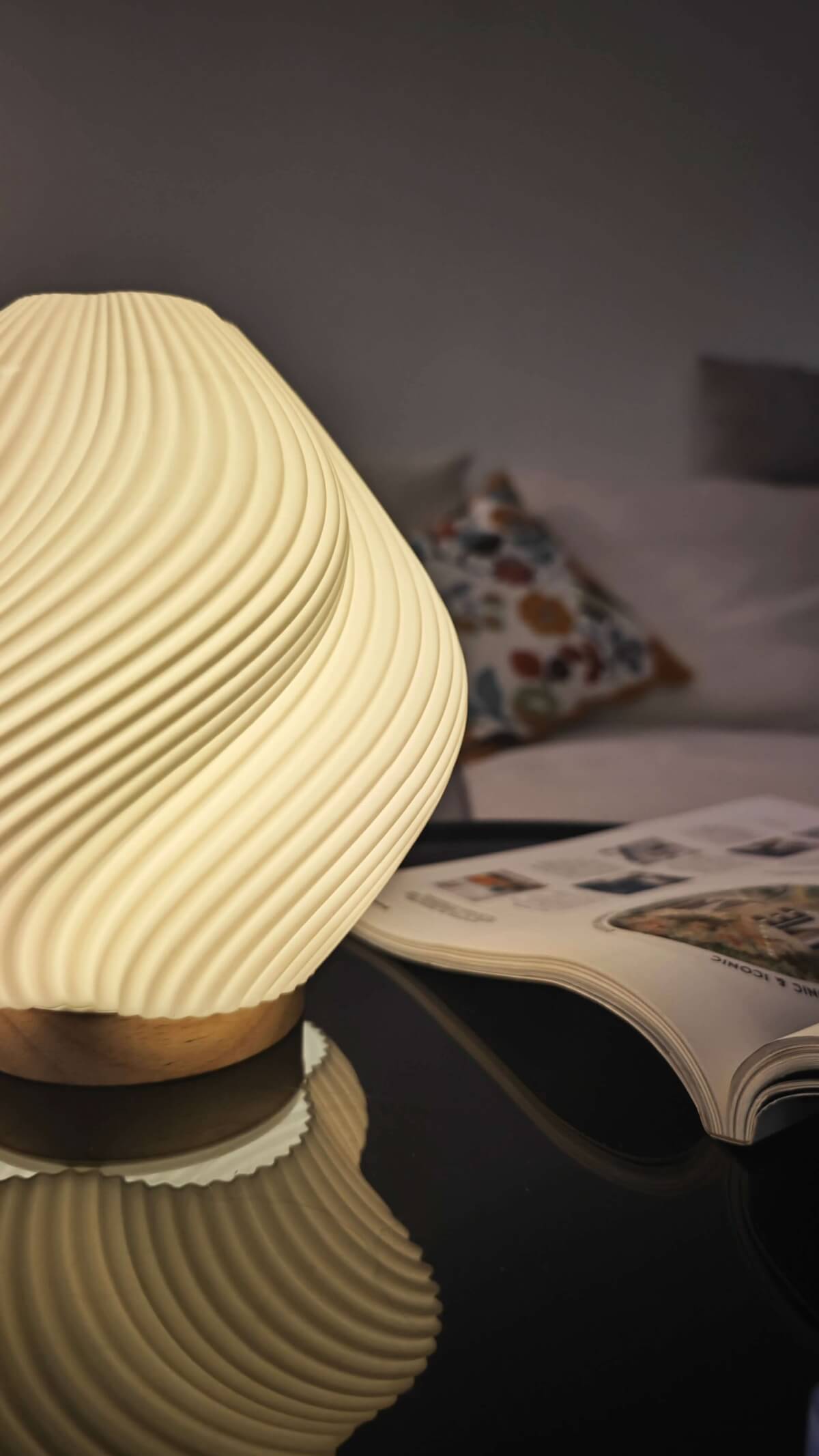 Whimsical Wave Table Lamp with cream shade, wood base, on black reflective surface, near a book.